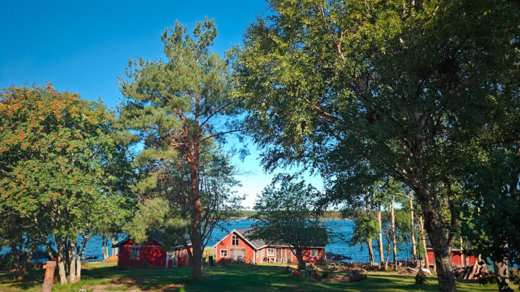 Röda trästugor bland gröna träd vid en blå sjö under en klar himmel.