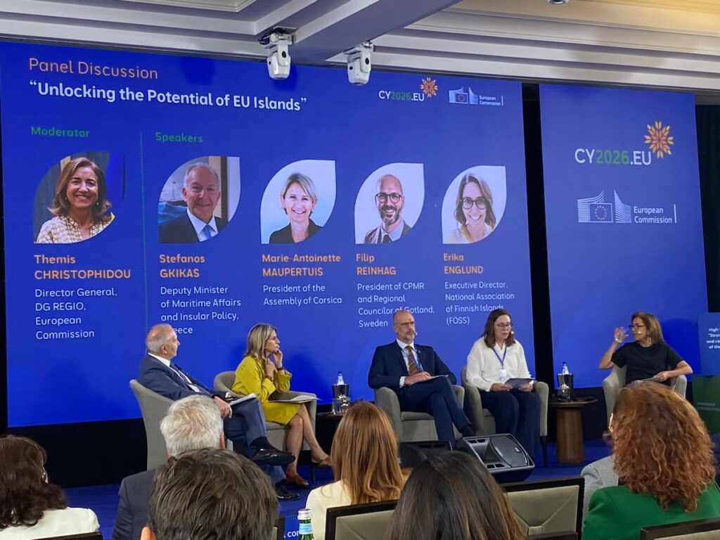 Paneldiskussion med titeln ”Att frigöra potentialen hos EU:s öar”, där fem talare sitter på scenen framför en digital skärm som visar deras porträttbilder och titlar.