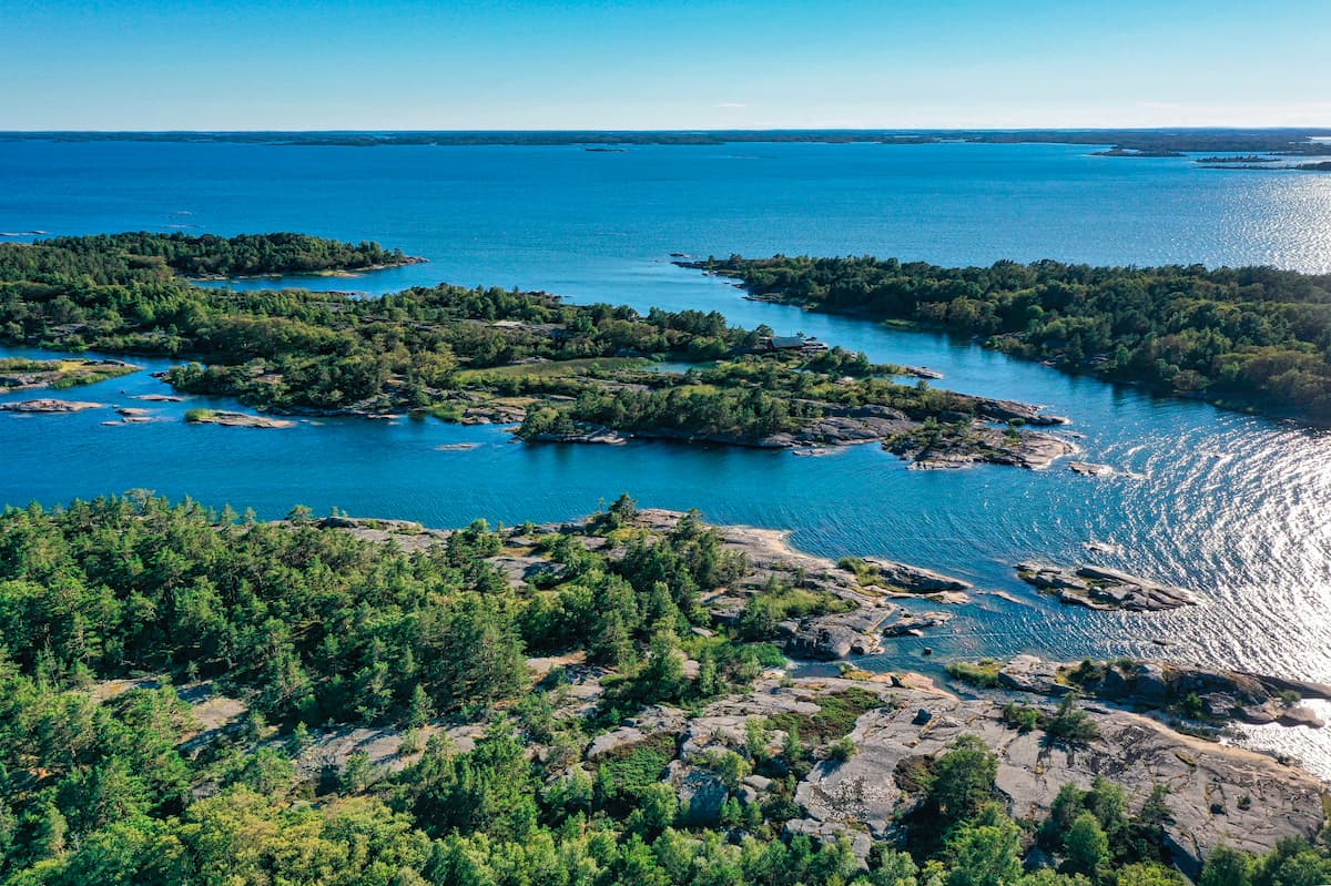 Flygbild över en kustnära skärgård med skogsklädda öar omgivna av djupblått vatten.